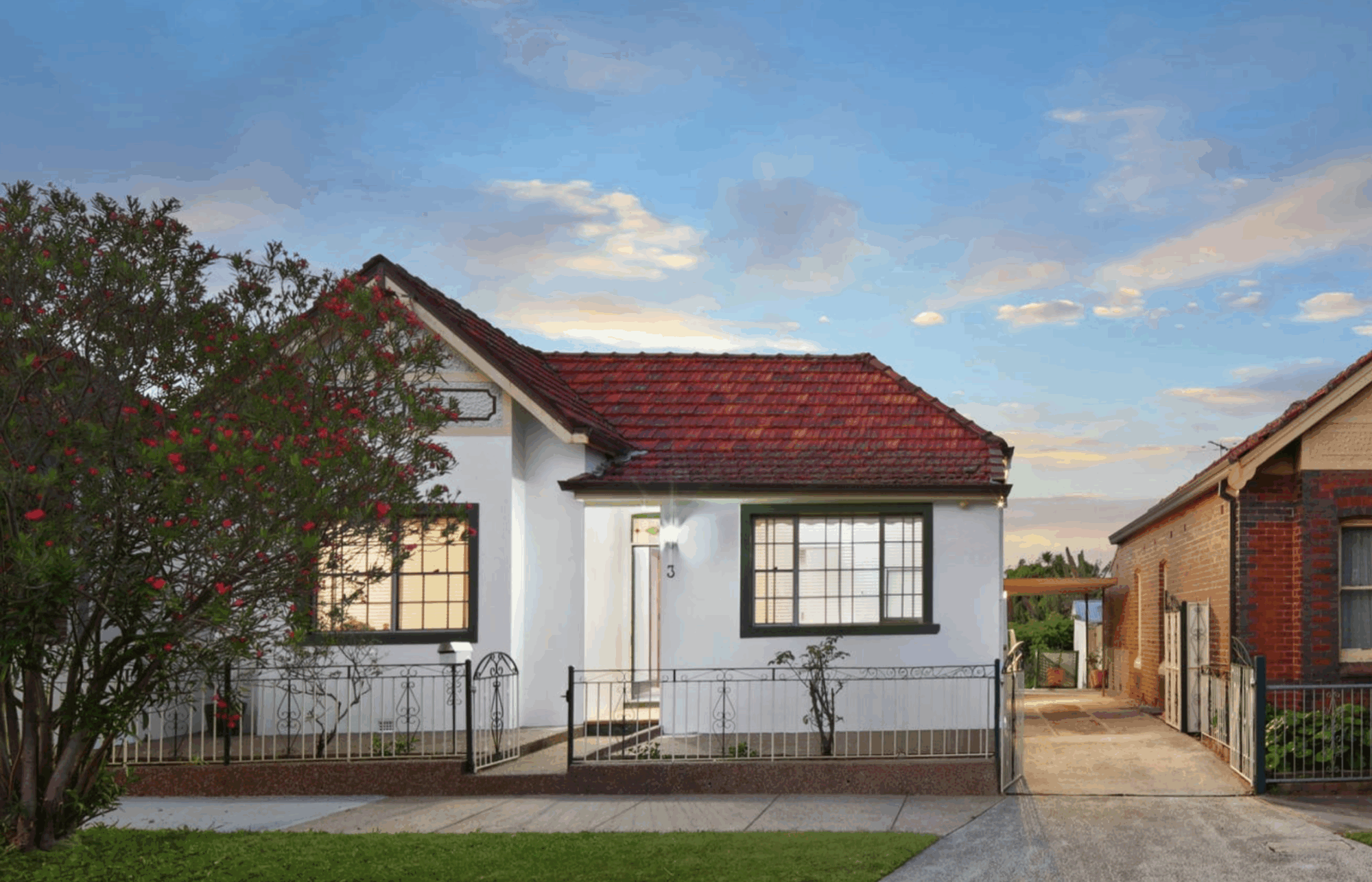 Cozy white house with red roof under a vibrant sky.